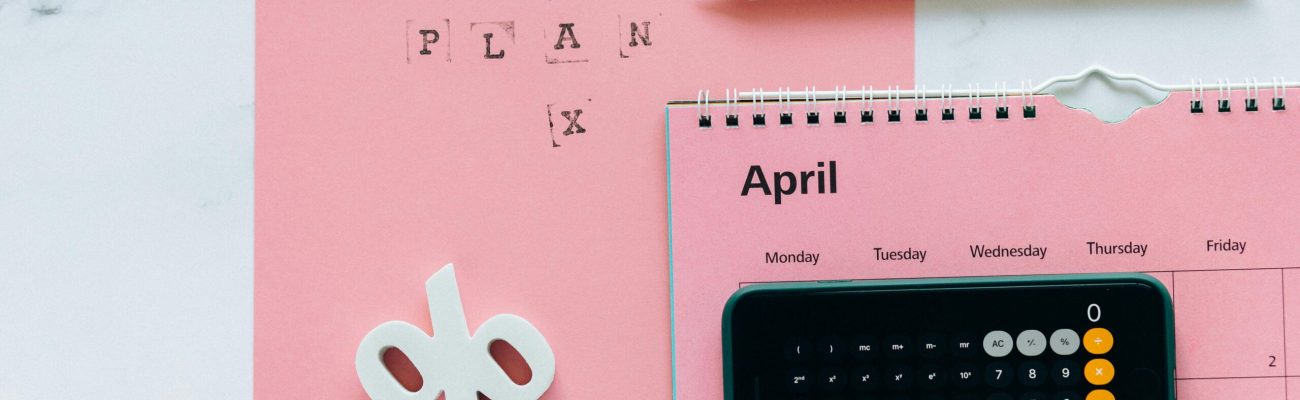 Flat lay of April calendar with calculator, pencil, and pink background for financial planning.