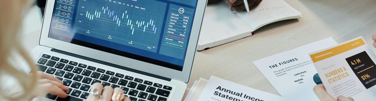 Business professionals analyzing financial data on a laptop during a meeting. Charts and reports visible.